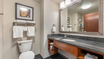 A modern bathroom with a toilet, sink, and large mirror. There are towels on the wall and shelves under the sink.