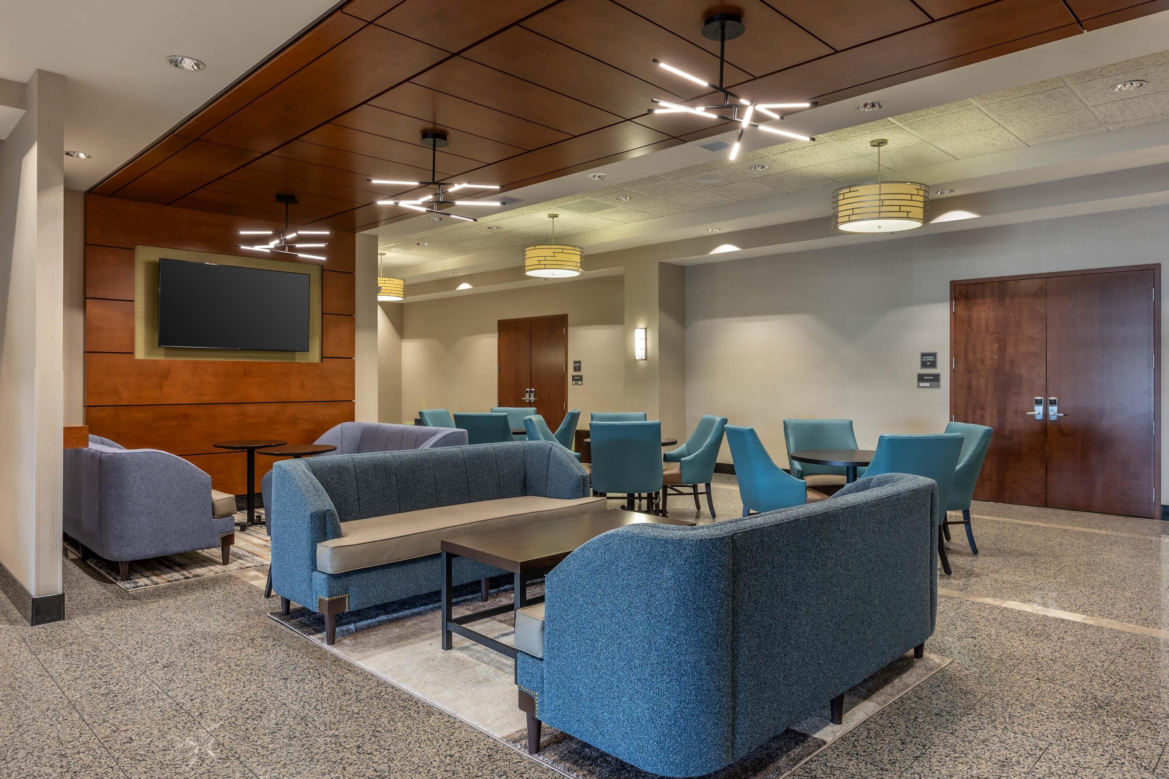 A modern lobby with seating areas, a flat-screen TV, and a wooden accent wall.