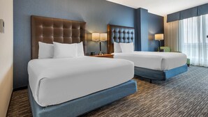 A hotel room with two beds, a large window with curtains, and a carpeted floor.