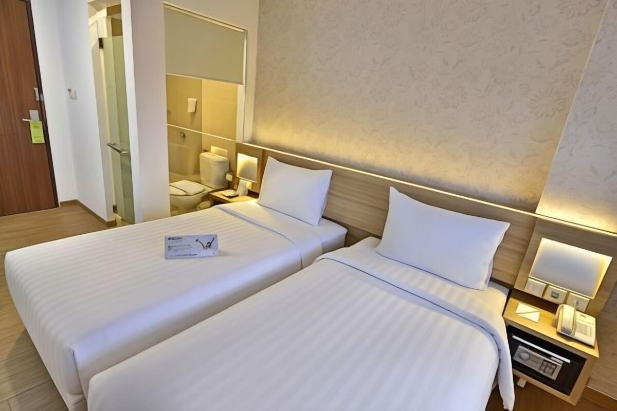 Una habitación de hotel con dos camas, un baño y una mesita de noche con lámpara y teléfono.