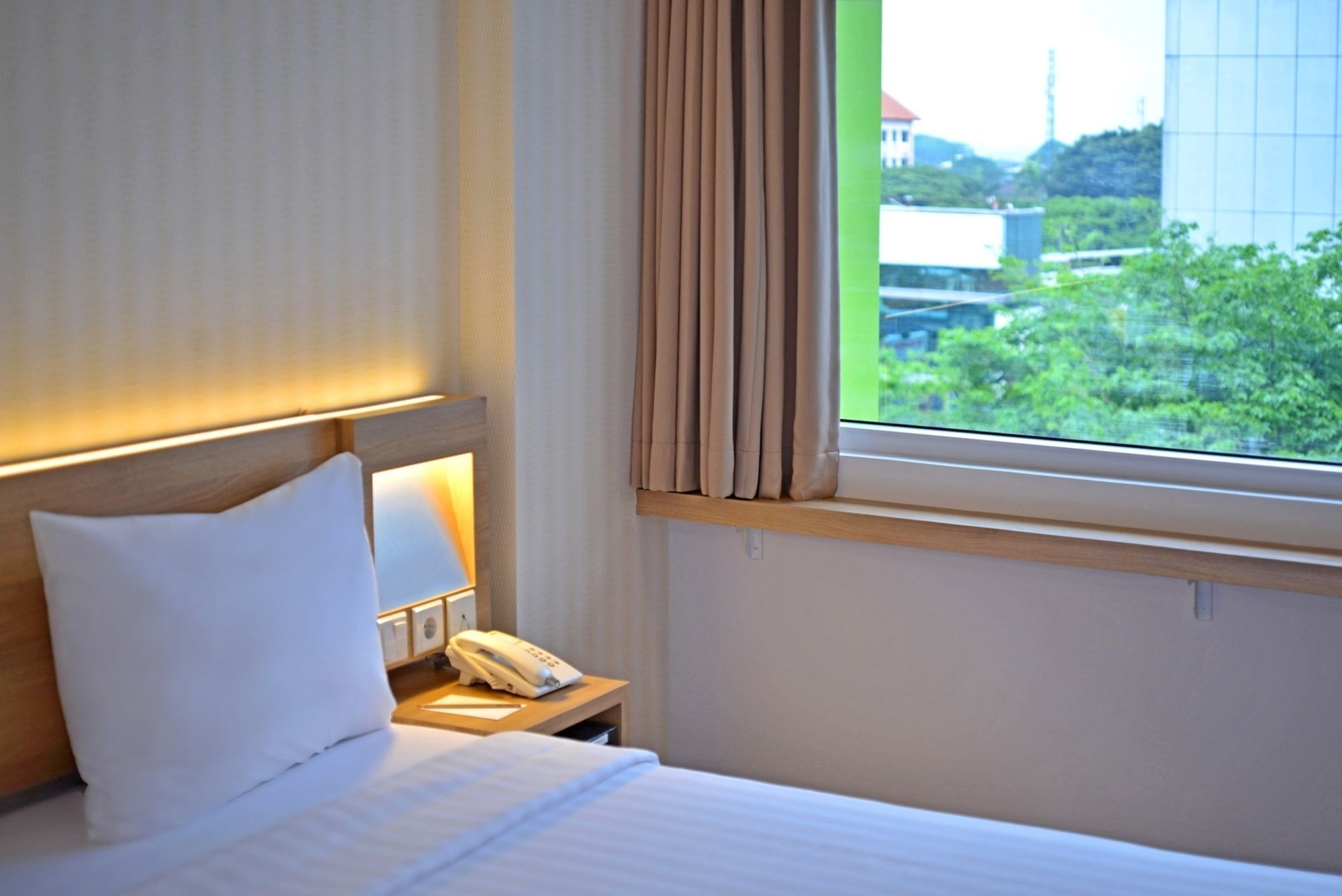 Une chambre d’hôtel avec un lit, une table de chevet avec une lampe, un téléphone et une fenêtre avec des rideaux.