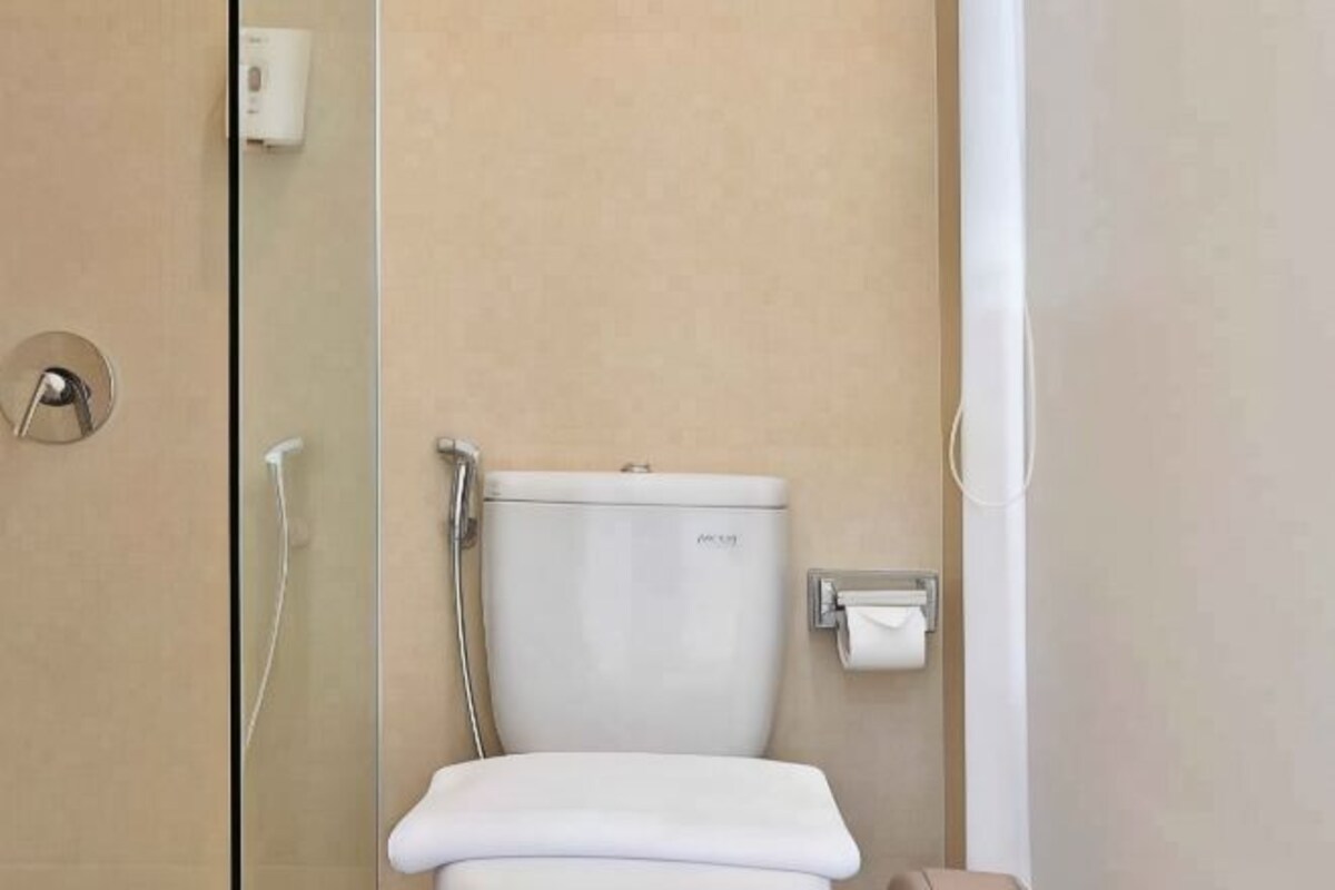 A modern bathroom with a toilet, a towel dispenser, and a glass shower enclosure.