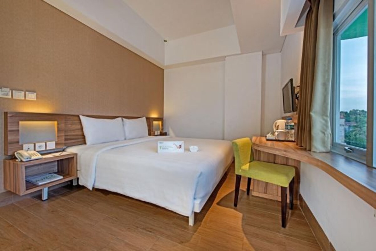 Habitación de hotel con una cama grande, mesita de noche con lámpara, una silla, escritorio con computadora y ventana con vistas.