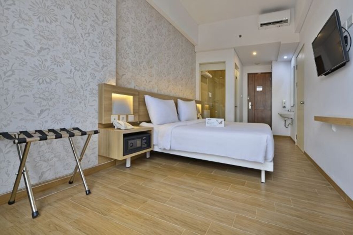 A hotel room with a bed, bedside table, lamp, TV, and a mirror.