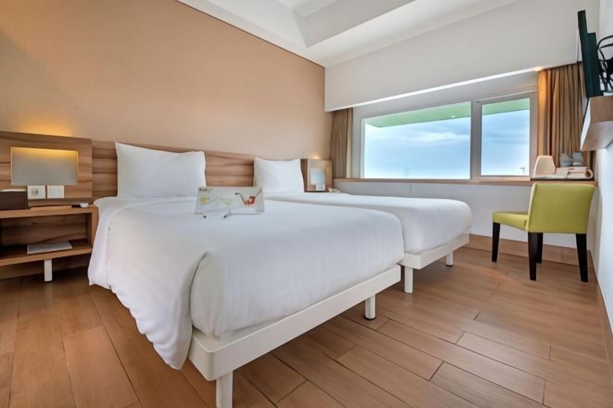 Habitación de hotel con dos camas, un escritorio, una silla, un televisor y una ventana con vistas.