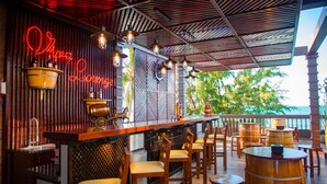 A bar area with wooden chairs and tables, a neon sign, and a view of the ocean. - Viva Beach Resort Mui Ne (Mui Ne)