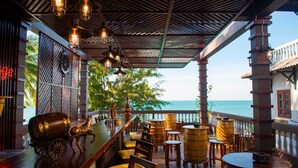 A bar area with wooden furniture, a horse carriage decoration, and a view of the ocean. - Viva Beach Resort Mui Ne (Mui Ne)