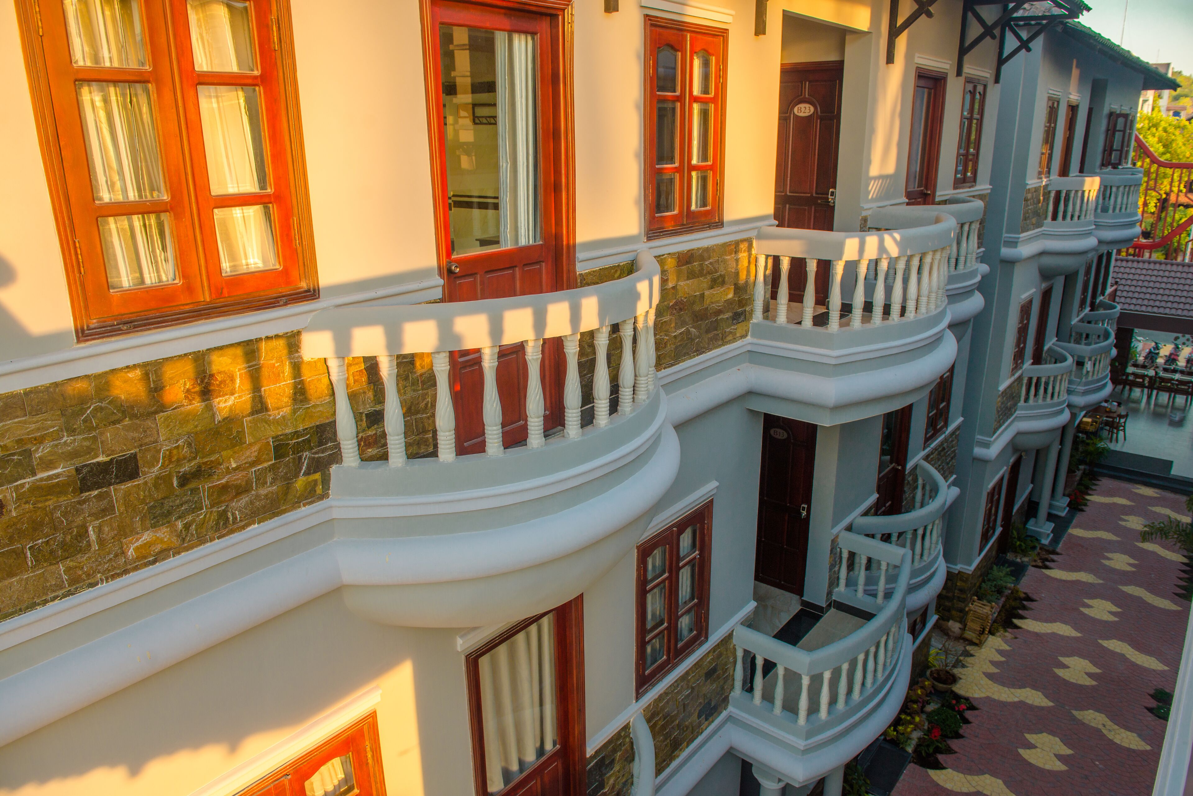A multi-story hotel with balconies, stone facade, and a patterned walkway.