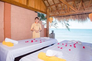 A spa room with two beds, each with a white sheet and towels, and a wooden ceiling.