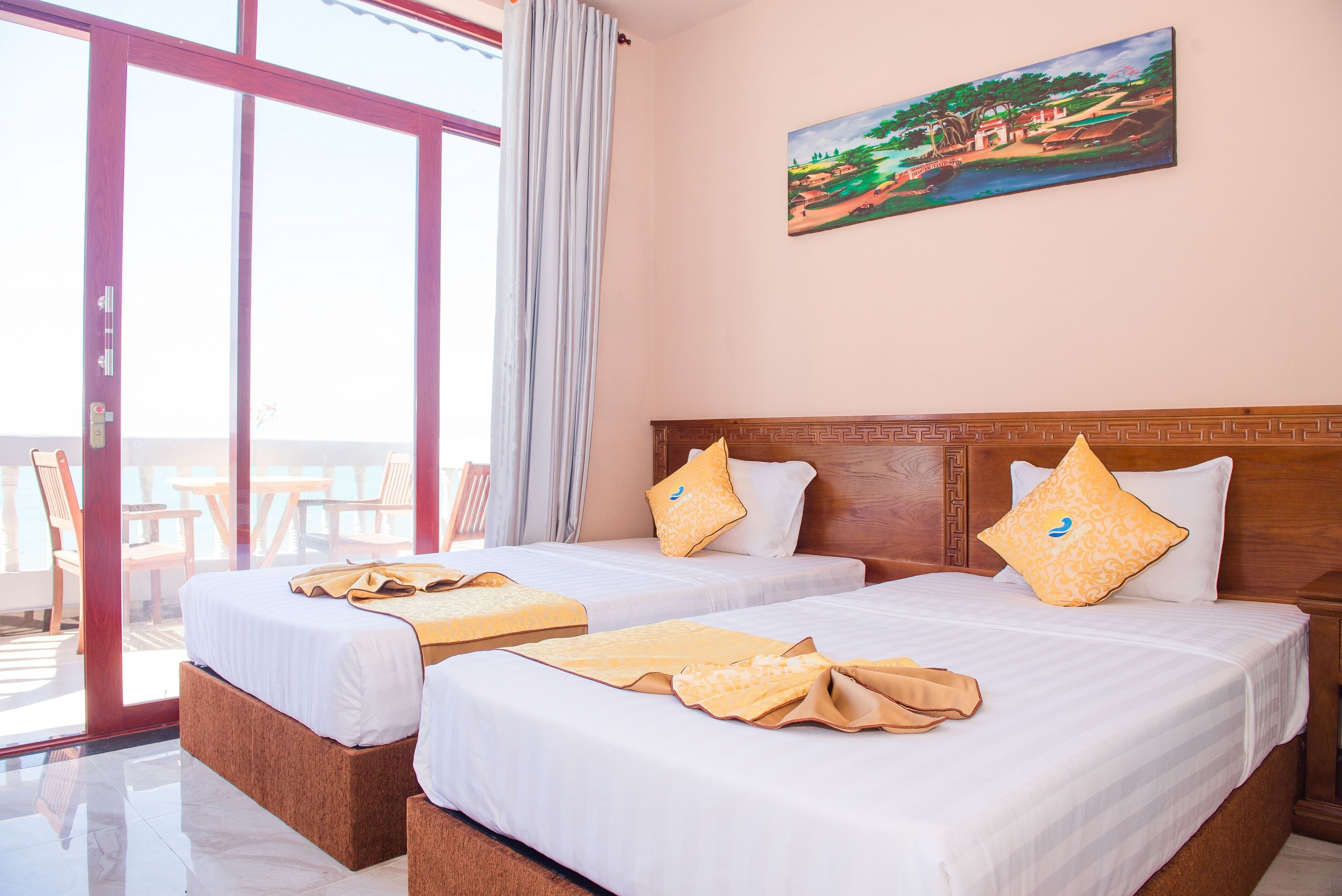 A hotel room with two beds, a painting on the wall, and a balcony with chairs.