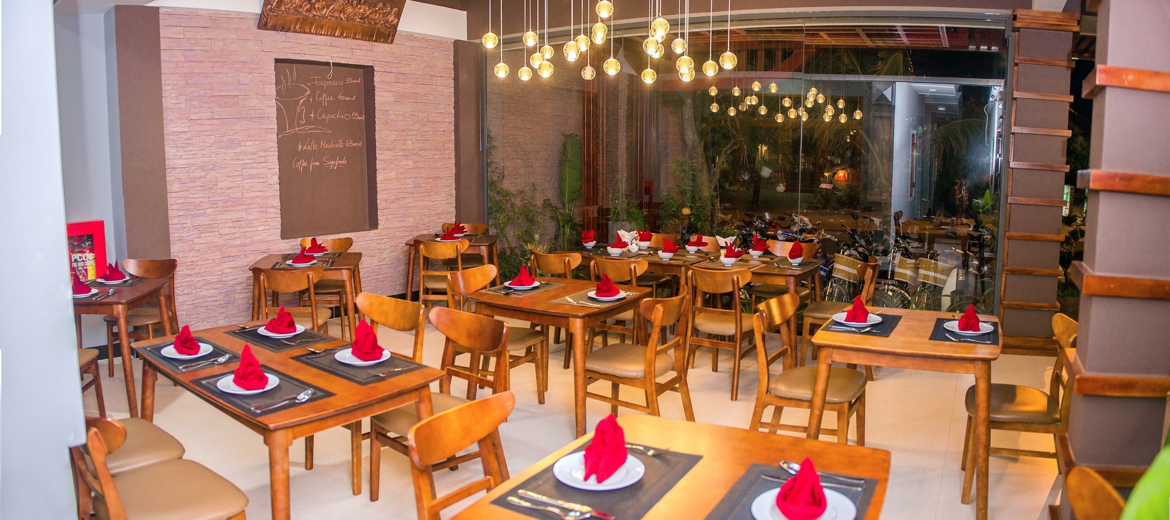 A restaurant with wooden tables and chairs, a chalkboard menu, and hanging pendant lights.