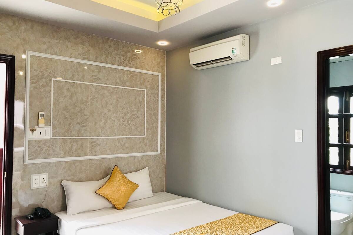 Une chambre d’hôtel comprenant un lit, une table de chevet avec un téléphone, un appareil de climatisation et un luminaire fixé au mur.