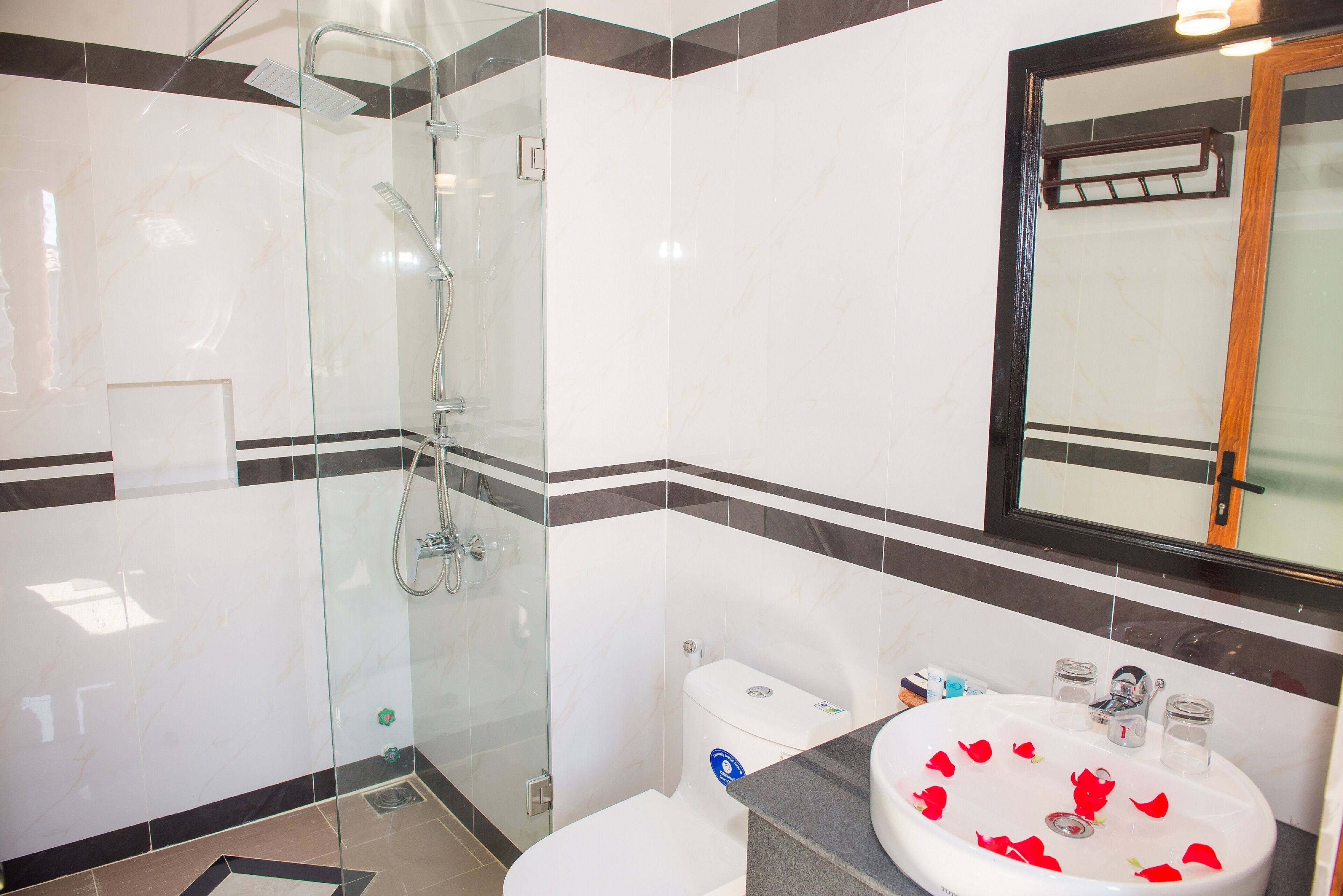 Un baño con ducha envuelta en vidrio, inodoro y lavamanos con pétalos de rosa.