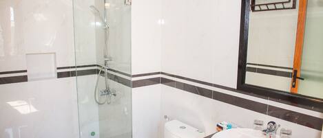 Un baño con ducha envuelta en vidrio, inodoro y lavamanos con pétalos de rosa.