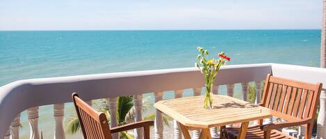Een houten tafel en stoelen op een balkon met uitzicht op zee.