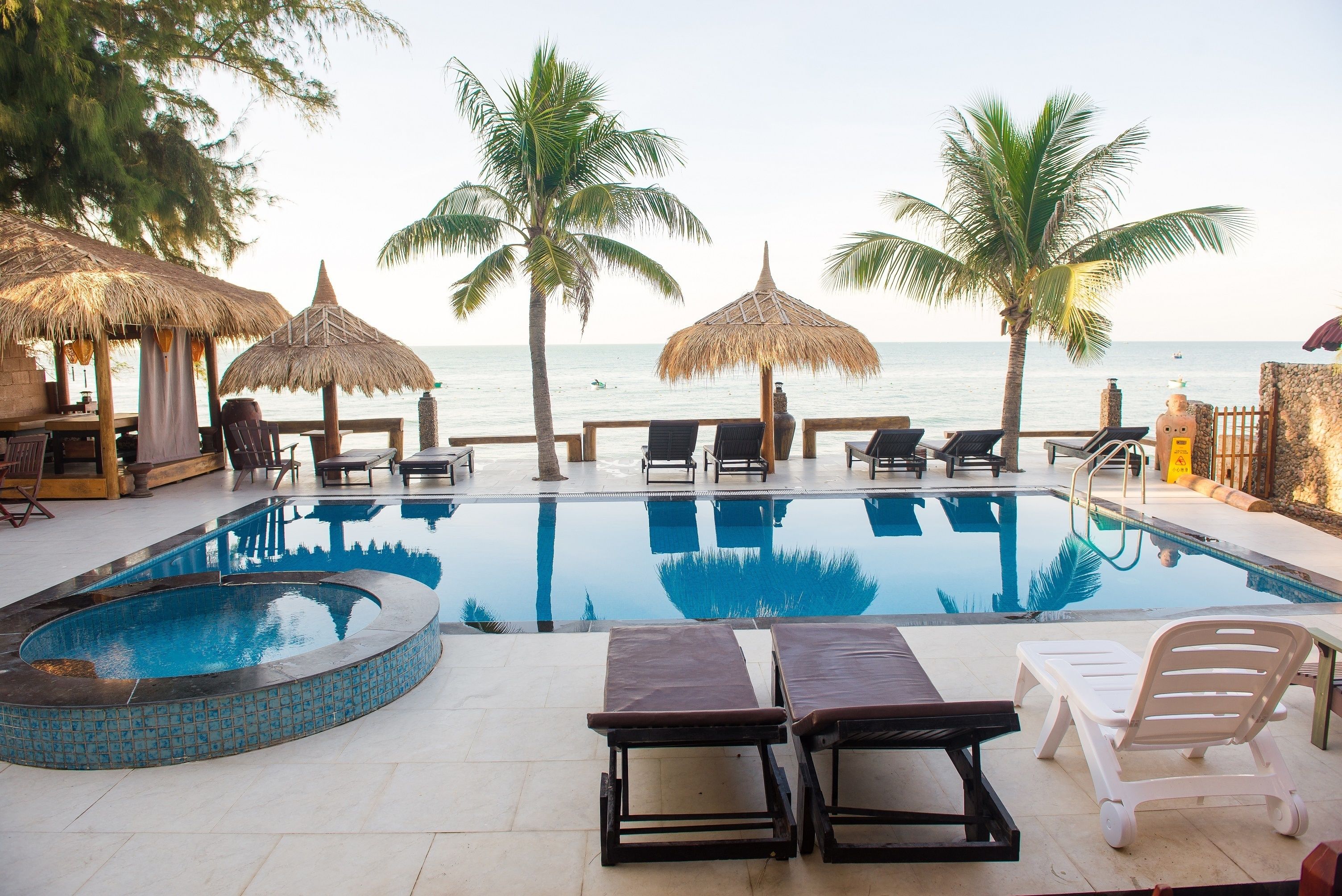 A poolside area with lounge chairs, a swimming pool, and palm trees.