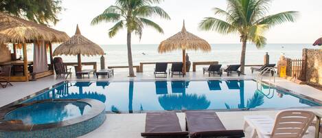 Un espace aménagé au bord de la piscine, avec des chaises longues, une piscine et des palmiers.