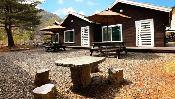 A rustic cabin with a gravel patio, picnic tables, and outdoor seating. - Planttrees House (Pyeongchang)