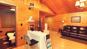 A cozy cabin interior with a wooden interior, a white desk with a coffee machine, a leather couch, and a small table with a lamp. - Planttrees House (Pyeongchang)