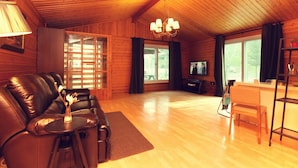A cozy living room with a leather sofa, a television, and a wooden dining area. - Planttrees House (Pyeongchang)