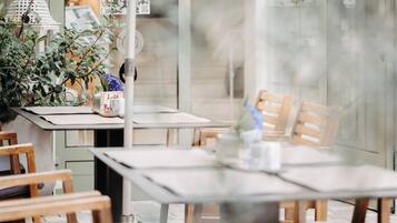 Un restaurante con sillas y mesas de madera, una planta en maceta y un panel de vidrio.