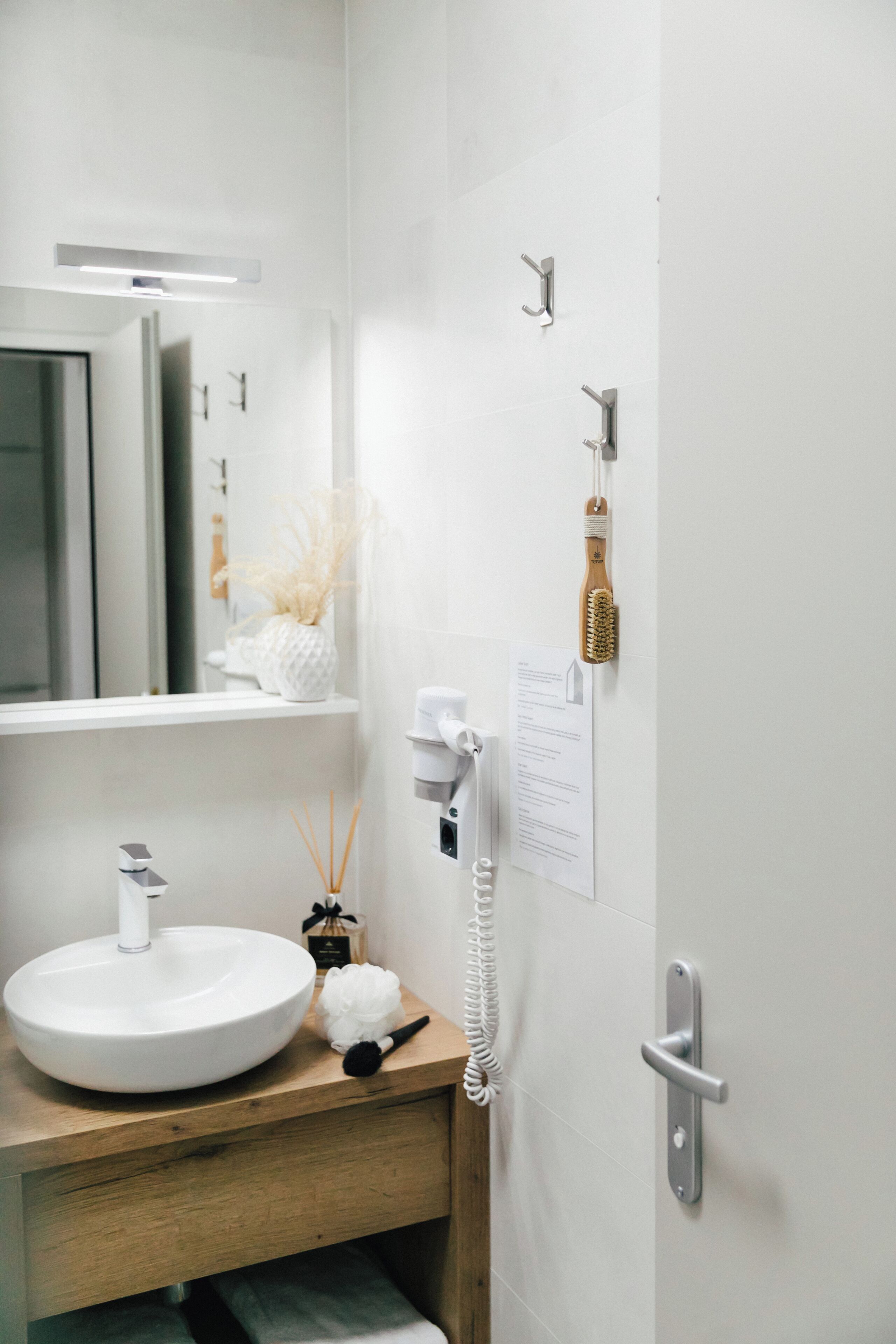 Un baño con lavamanos blanco, espejo, soporte para cepillos de dientes, secador de pelo y toallero.