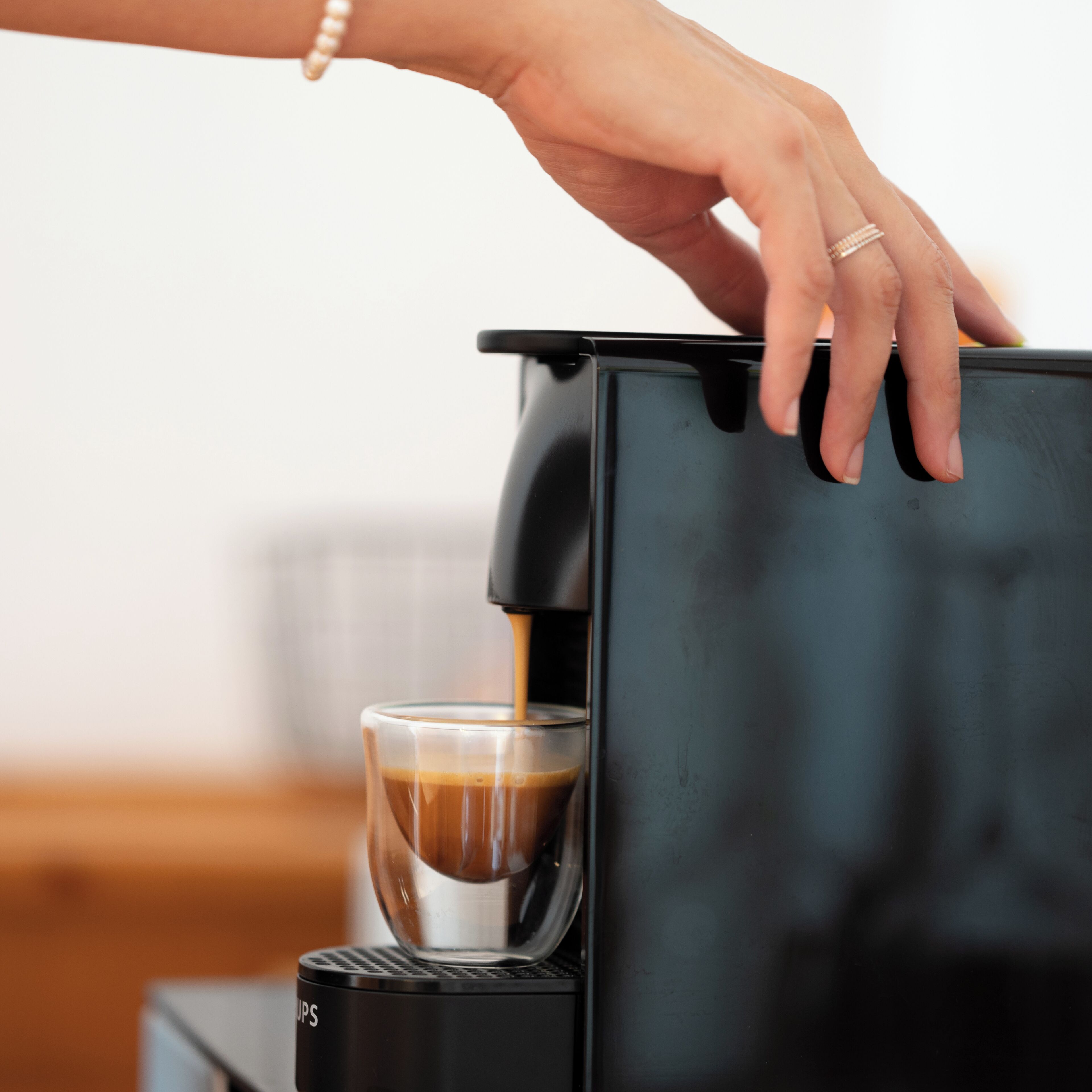 Una mano operando una cafetera, sirviendo café en un vaso.