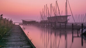 Un muelle de madera que conduce a un puerto deportivo con varias embarcaciones y un edificio al fondo.