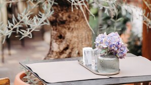 A table with a vase of flowers and a glass, set against a backdrop of a large tree. - Das Stadthaus (Neusiedl am See)