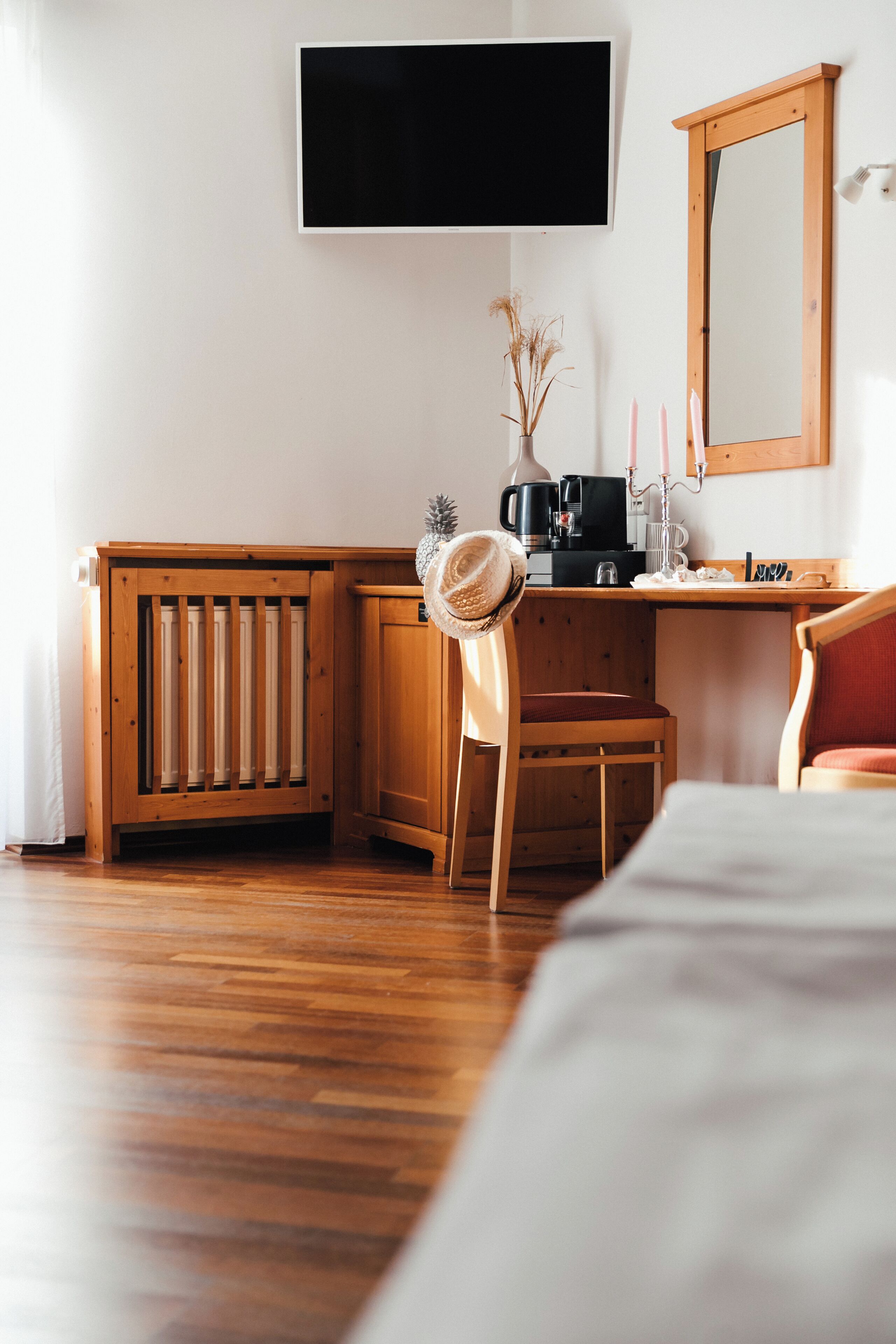 Una stanza con una scrivania in legno, una sedia, un letto, una TV a parete e uno specchio.