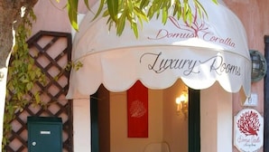 The entrance to Domus Corallia Luxury Rooms, featuring a welcoming archway, a small reception area with a vase of sunflowers, and a decorative coral sign.