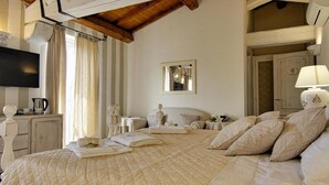 A bedroom with a large bed, a flat-screen TV, a bedside table with a lamp, and a window with curtains.