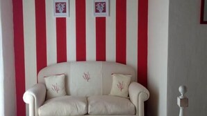 A room with a beige sofa against a red and white striped wall, two framed pictures, and a wooden bed frame.