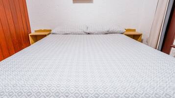 Una cama bien hecha con una colcha estampada, mesitas de noche de madera y un pequeño cuadro en la pared.