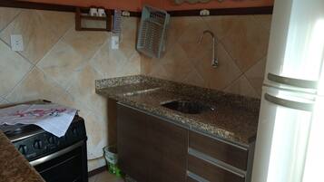 A kitchen with a granite countertop, stainless steel sink, and a refrigerator.