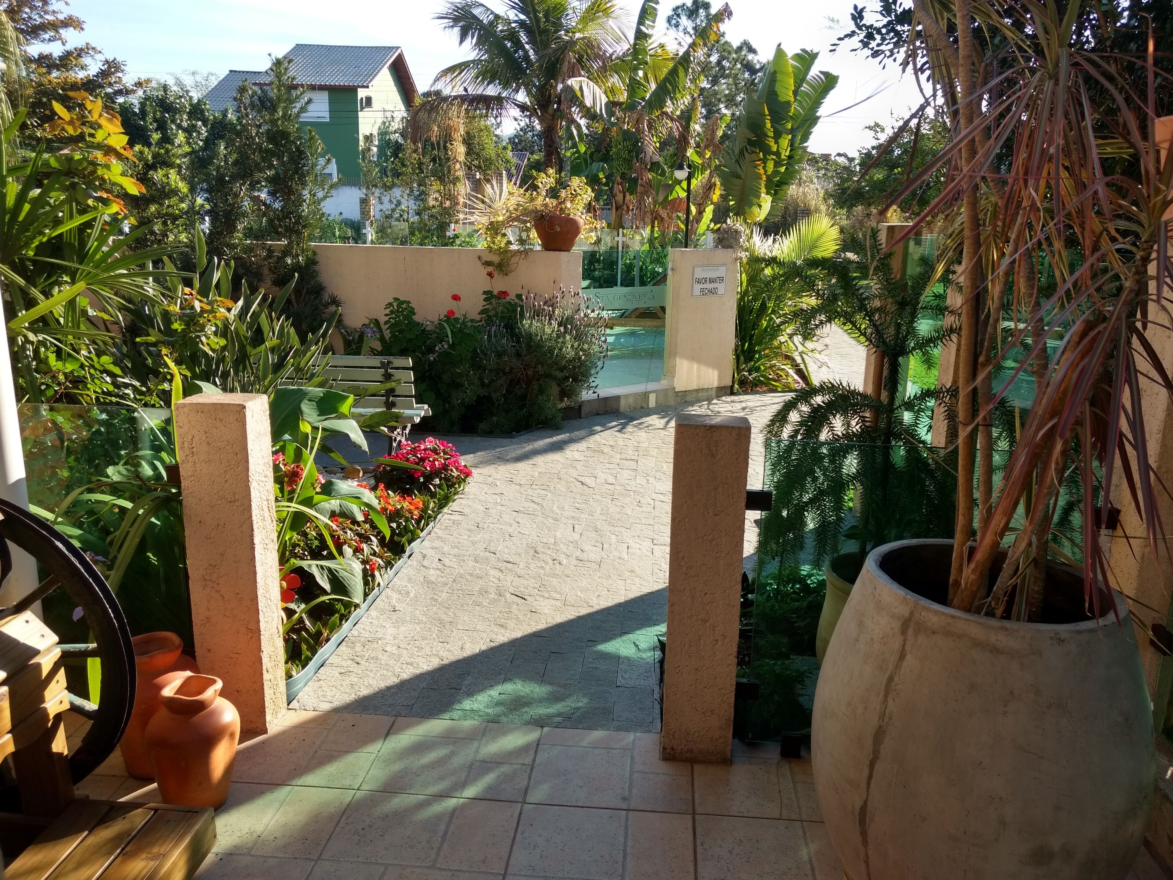 A garden pathway leading to a bench with potted plants and a sign.