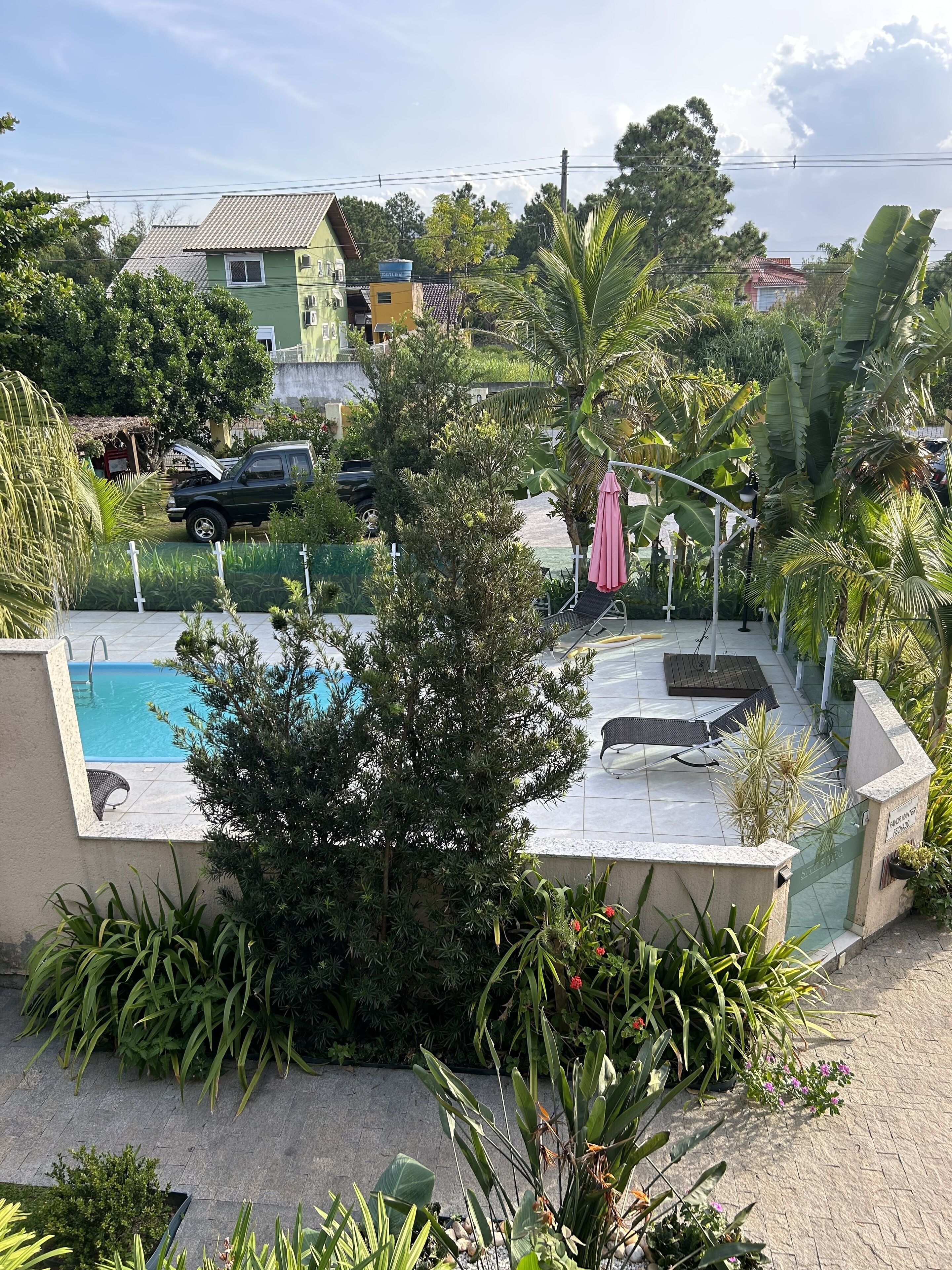 Zona residencial amb una piscina, envoltada de vegetació exuberant i poques cases al fons.
