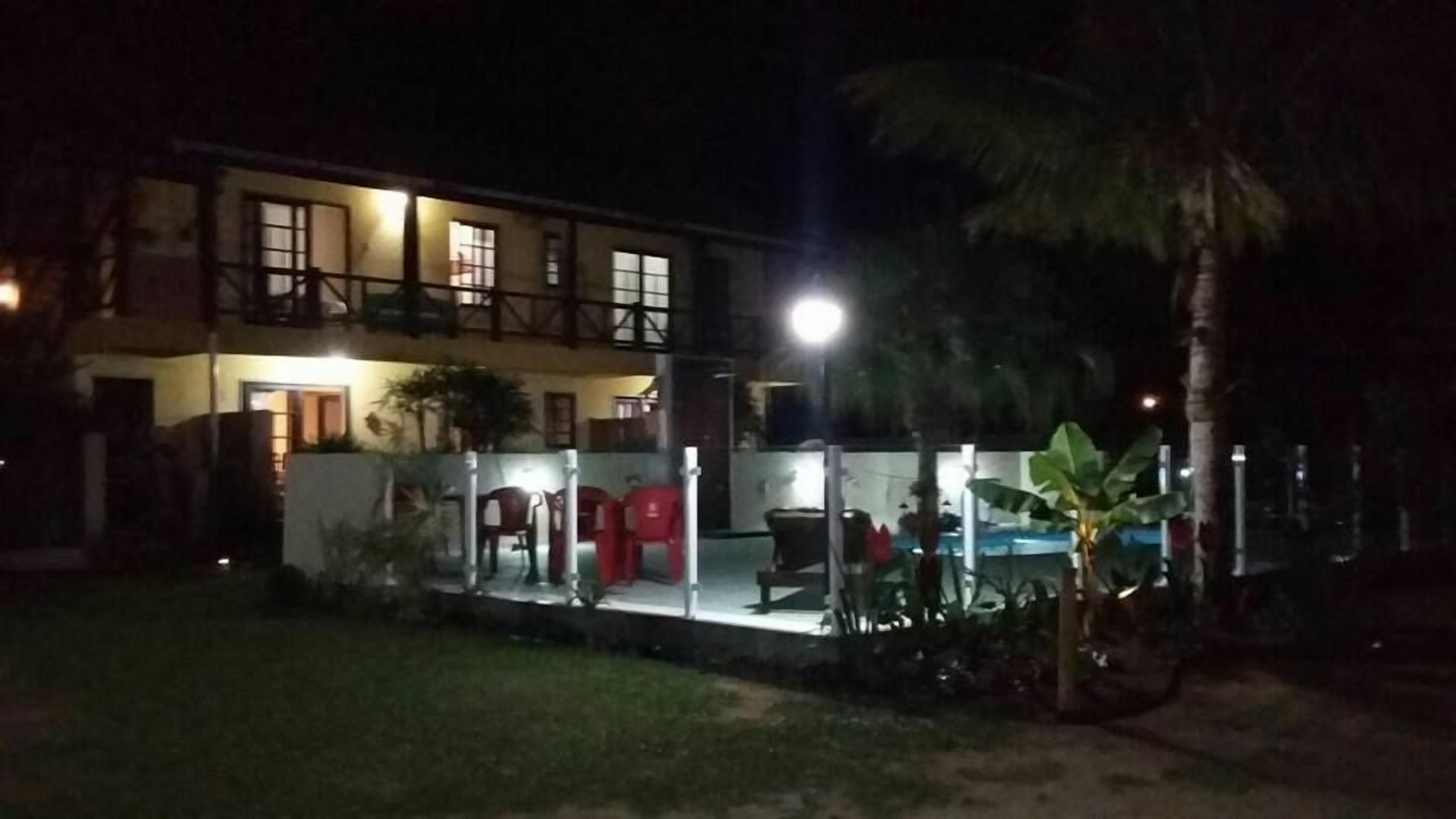 A two-story building with a balcony and a well-lit outdoor area with chairs and a table.