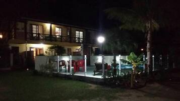 A two-story building with a balcony and a well-lit outdoor area with chairs and a table.