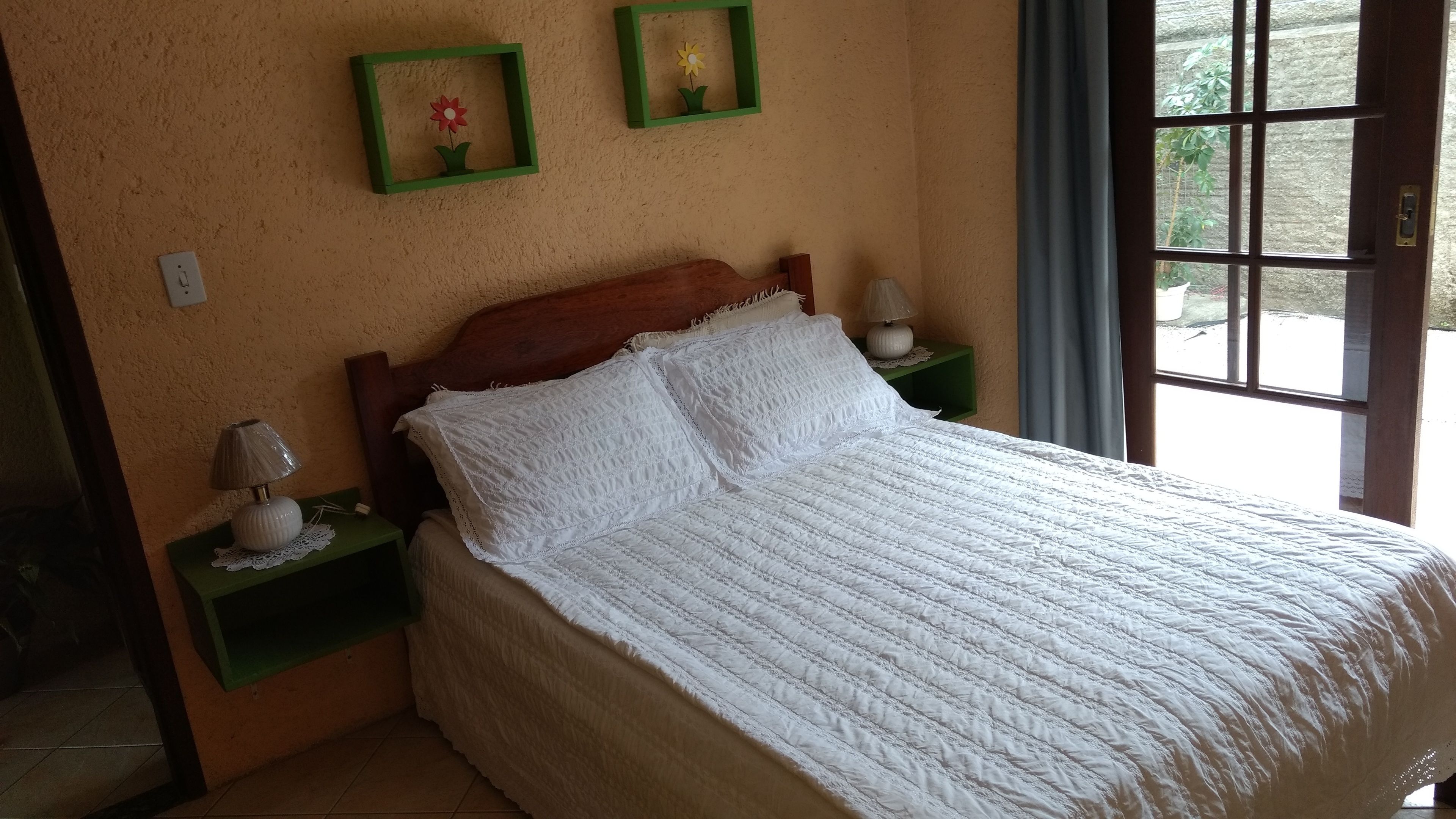 A neatly made bed with white bedding, a wooden headboard, and two bedside tables with lamps. There are two framed pictures on the wall above the bed.