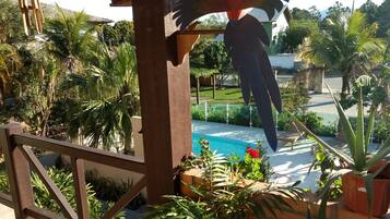 Zona de piscina con una pérgola de madera, plantas en macetas y vistas a un barrio residencial.