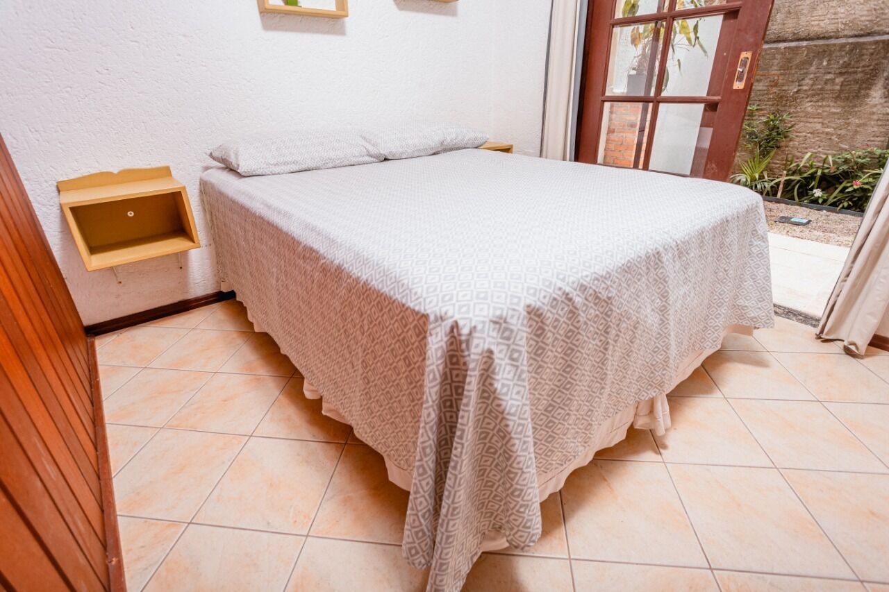 Uma cama de solteiro com um cobreleito estampado num quarto com chão de azulejos e um banco de madeira.