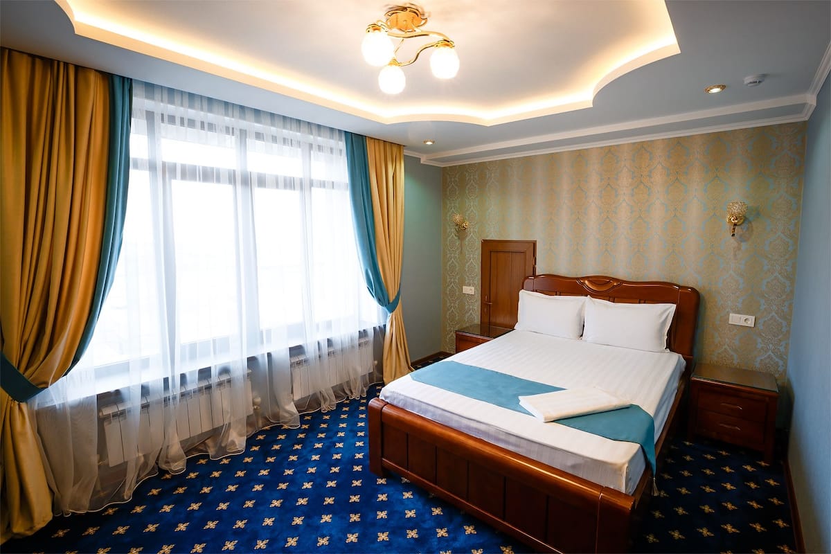 A hotel room with a bed, curtains, a patterned carpet, and a ceiling light fixture.