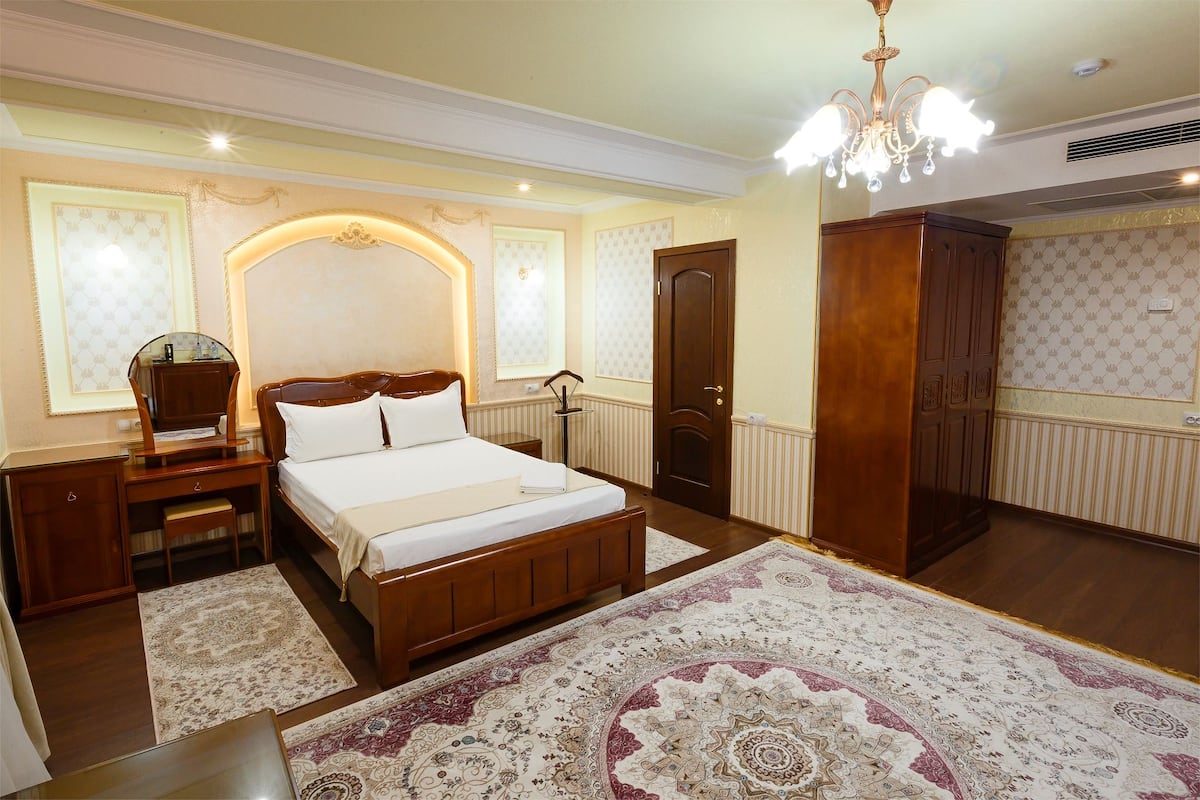 A hotel room with a wooden bed, a nightstand, a dresser, and a large patterned rug.