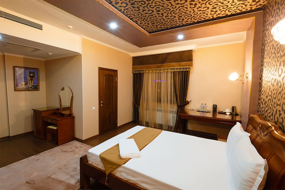 A hotel room with a bed, a desk, a chair, a mirror, and a radiator.