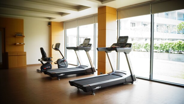 A gym with treadmills and elliptical machines, large windows, and a wooden floor. - Kiranshree Grand (Guwahati)
