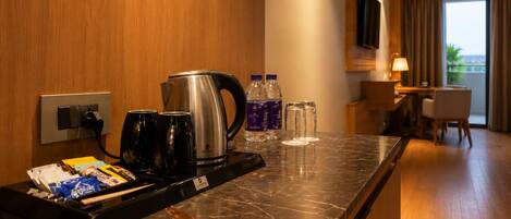 A hotel room with a marble countertop, a kettle, coffee cups, water bottles, and a minibar.