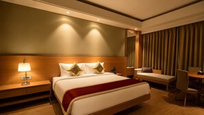 A hotel room with a large bed, bedside tables, a desk, and a chair. - Kiranshree Grand (Guwahati)