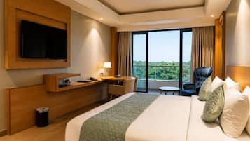 A hotel room with a bed, a desk, a chair, a TV, and a view of the outdoors.