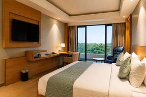 Habitación de hotel con cama, escritorio, silla, televisor y vistas al exterior.
